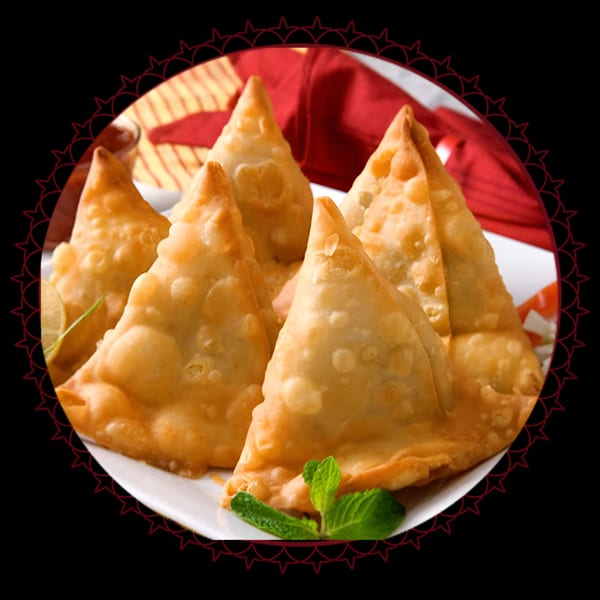 Golden-brown samosas, garnished with mint, on a white plate with a red napkin in the background.
