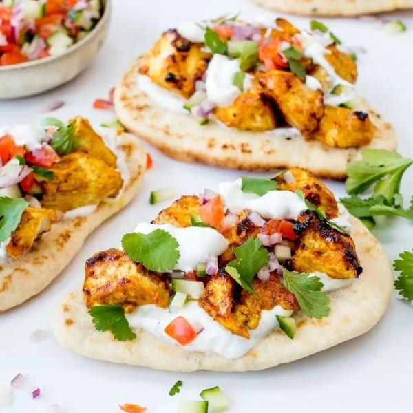 Three Tikka Curry & Grill chicken tikka flatbreads with yogurt, salsa, and cilantro on a white surface.
