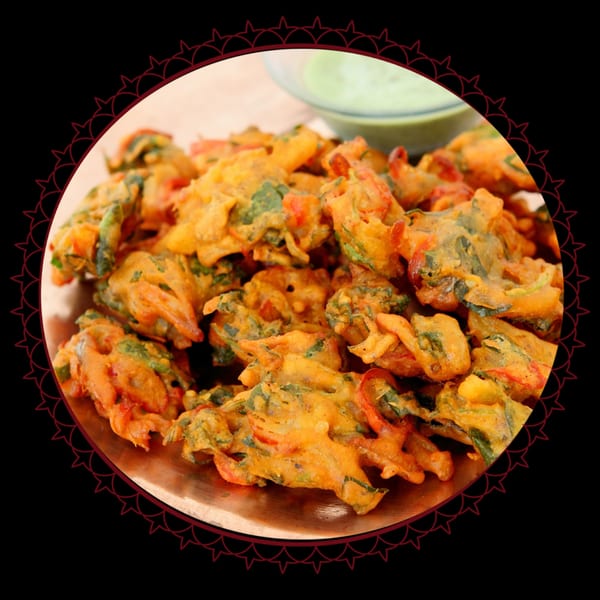 A copper plate filled with golden-brown pakoras, with a small bowl of green chutney in the background.