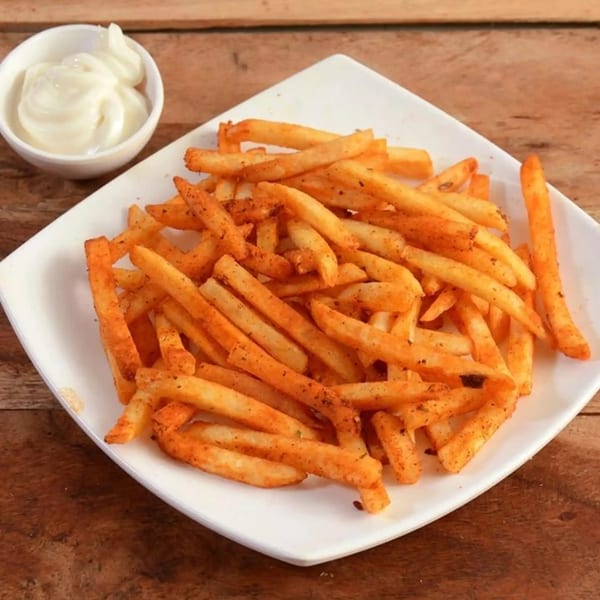 A plate of golden, seasoned French fries with a side of white dipping sauce on a wooden table.